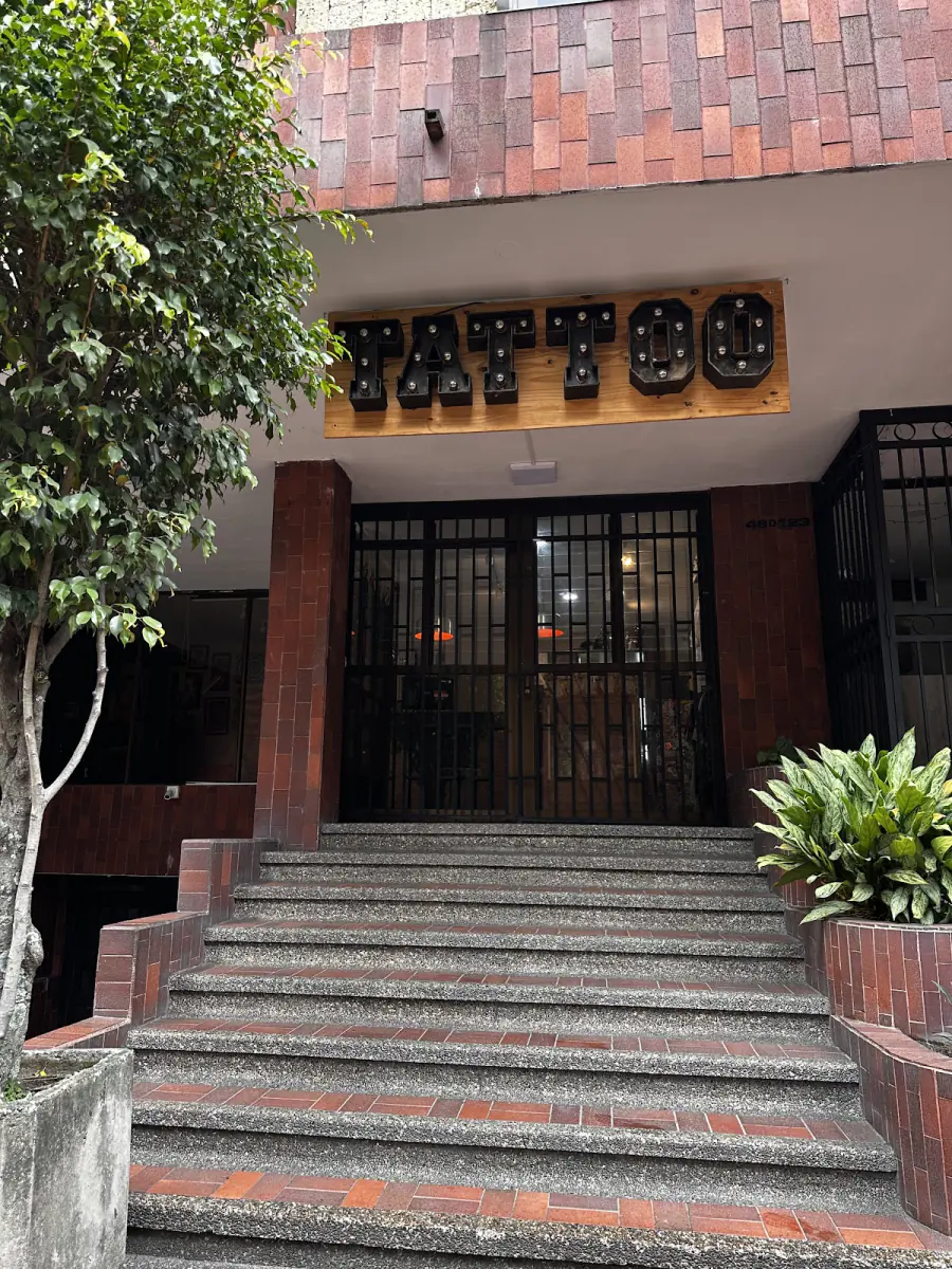 Entrada del estudio con escaleras, plantas y el letrero Tattoo